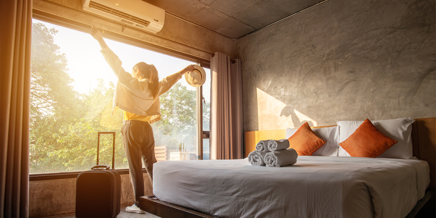 DREAMWAY TRAVEL Gast In einem Hotelzimmer steht eine Frau mit ausgebreiteten Armen am Fenster neben ihrem Bett