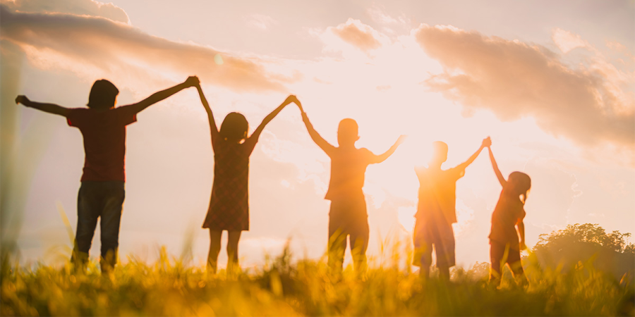 Fünf Kinder stehen nebeneinander auf einem Feld und halten sich an den Händen, die sie in die Luft halten