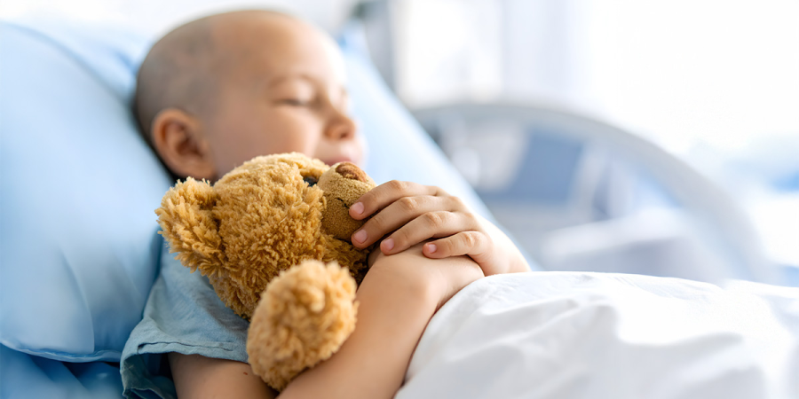 Ein Kind liegt schlafend in einem Krankenhausbett und hält einen Teddybär in der Hand