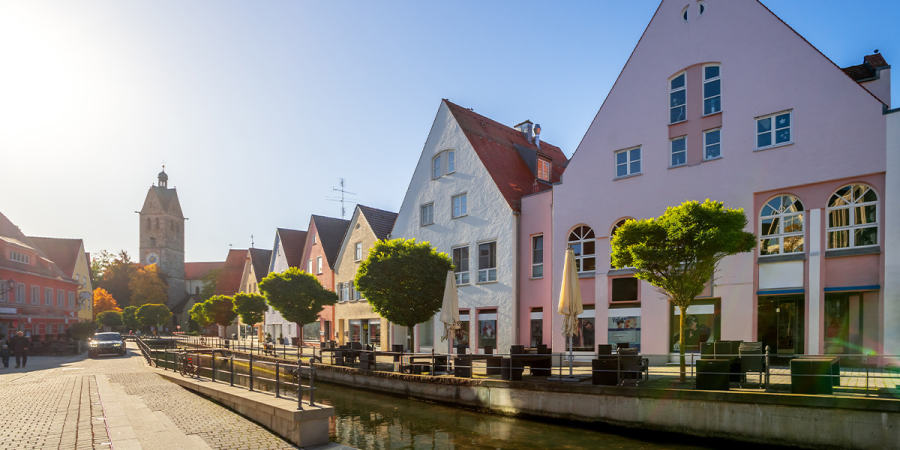 Eine Reihe von Gebäuden an einem Bach eine Kirche im Hintergrund, in Memmingen