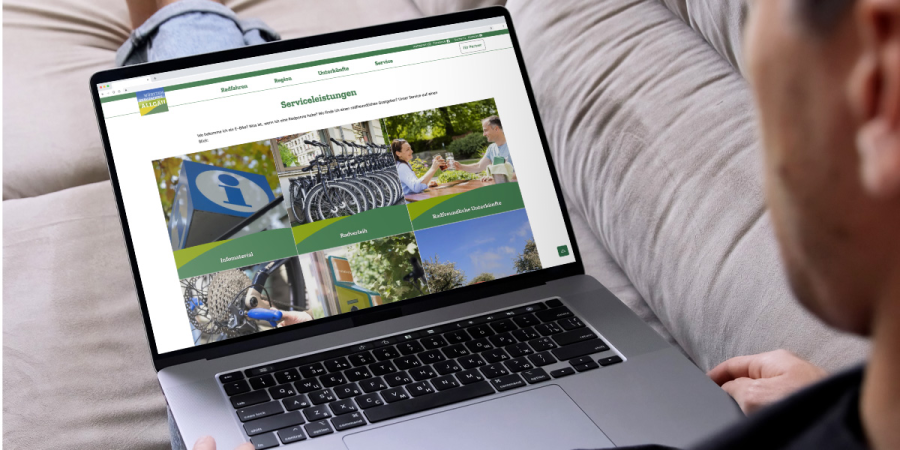 Ein Mann sitzt mit seinem Laptop auf dem Sofa und sieht sich die Website des Württembergischen Allgäus an