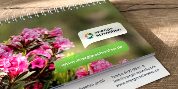 Tischkalender mit pinken Blumen auf der Titelseite liegt auf einem Tisch