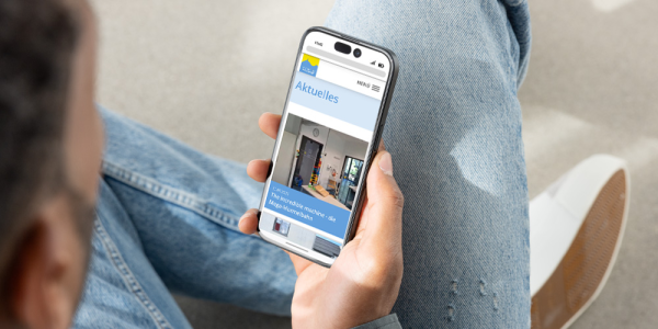 Ein Mann sitzt auf dem Boden und sein Smartphone in der Hand auf dem er sich die Website des Gymnasiums Immenstadt ansieht