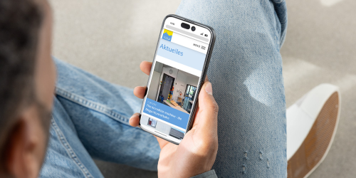 Ein Mann sitzt auf dem Boden und sein Smartphone in der Hand auf dem er sich die Website des Gymnasiums Immenstadt ansieht
