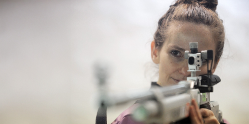 Eine Frau hält ein Gewehr in der Hand und zielt damit